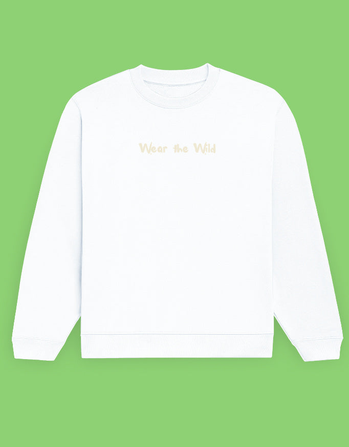 A white crewneck sweatshirt with 'Wear the Wild' printed in a light beige font on the chest, displayed against a solid light green background.