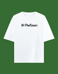 A white short-sleeve crewneck t-shirt with the text 'Be The CausE' printed across the chest in black script and green block letters, displayed against a solid dark green background.