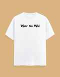 A white short-sleeve crewneck t-shirt with the phrase 'Wear the Wild' printed in black across the chest, displayed against a solid tan background.