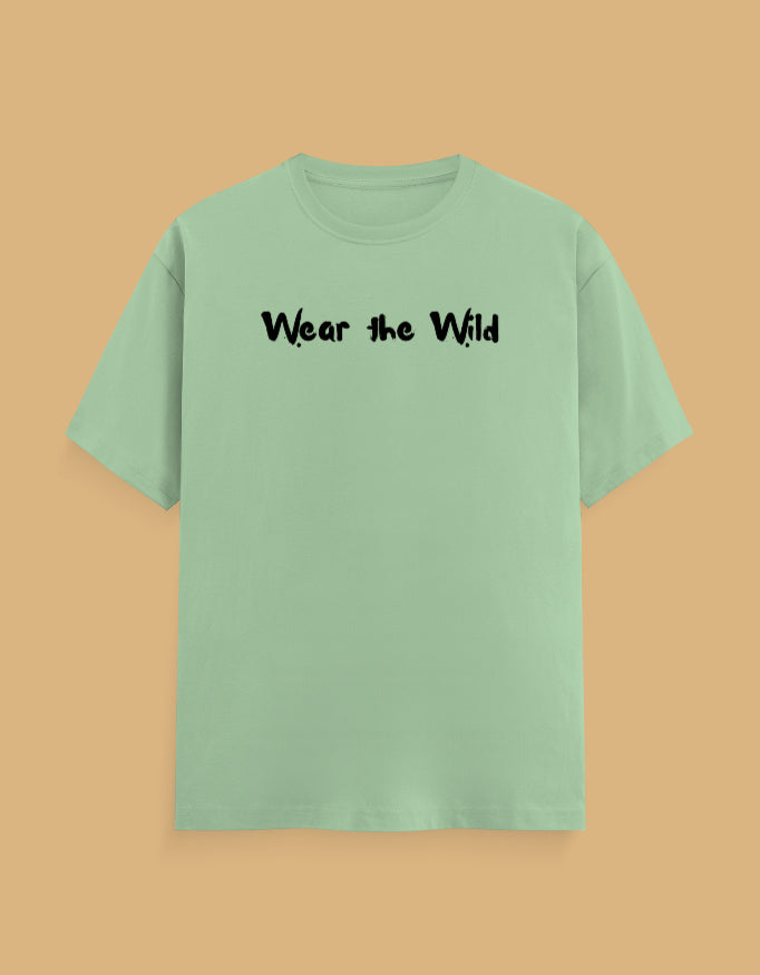A sage green short-sleeve t-shirt with the phrase 'Wear the Wild' printed in black across the chest, displayed against a solid tan background.