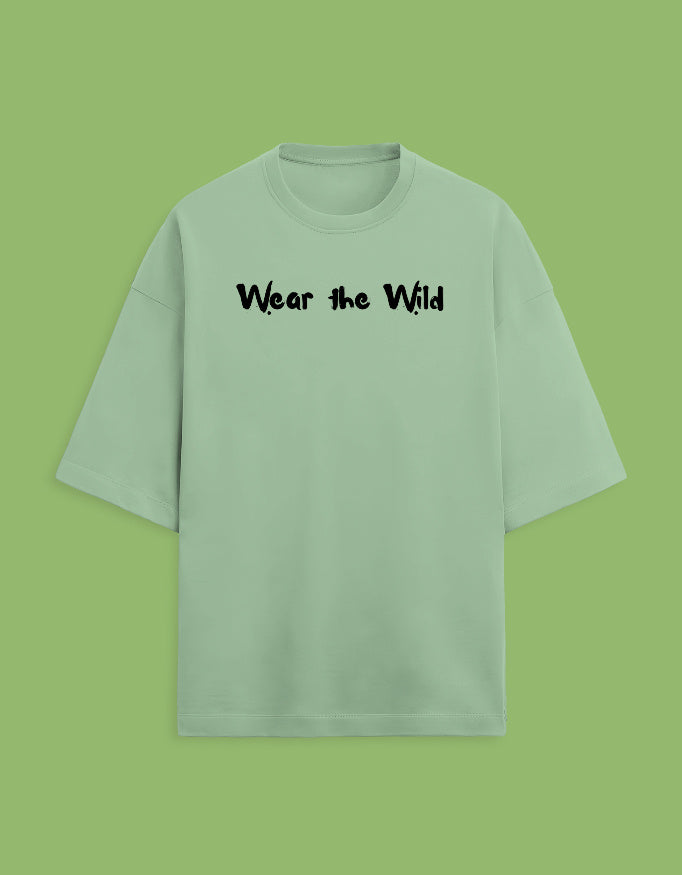 A light sage green short-sleeve t-shirt with the phrase 'Wear the Wild' printed in black across the chest, displayed against a solid light green background.