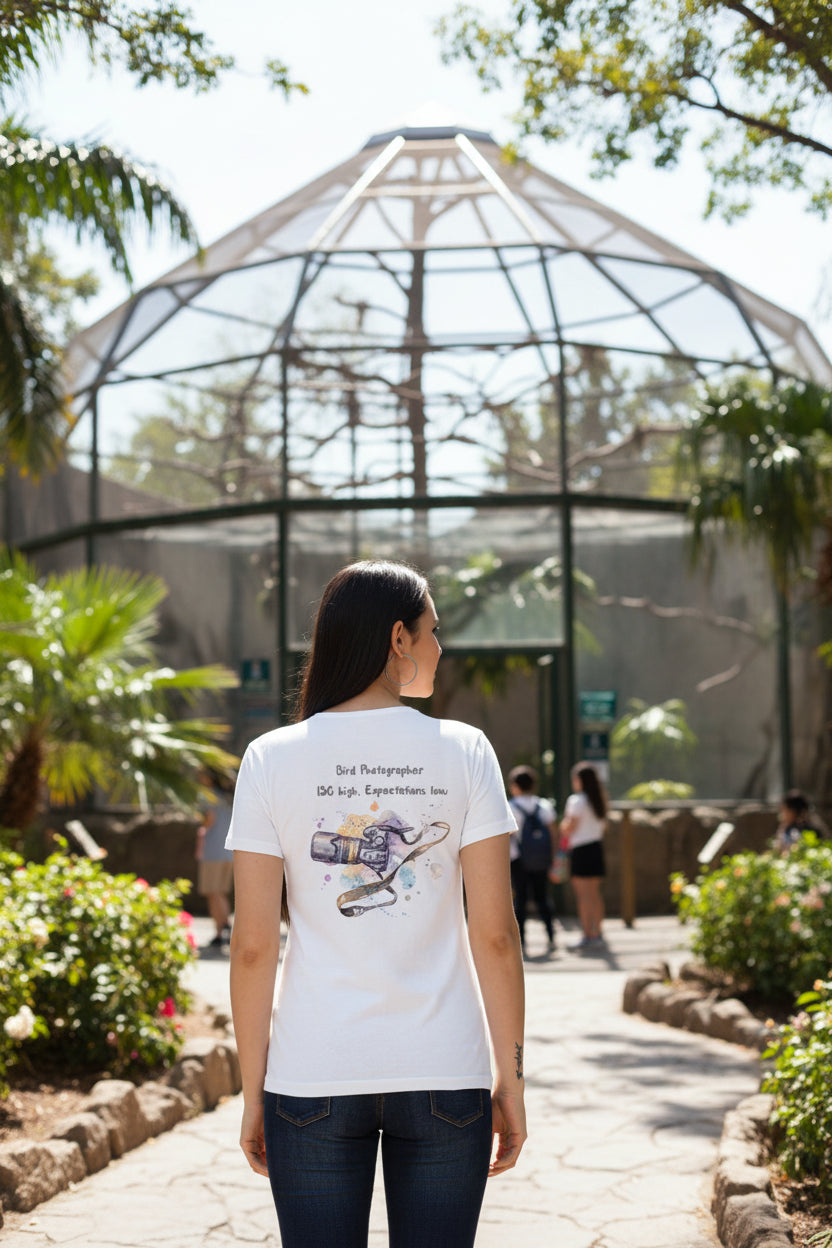 A woman shown from the back wearing a white short-sleeve T-shirt with a bird photographer graphic on the back, paired with dark blue jeans against a light gray studio background.